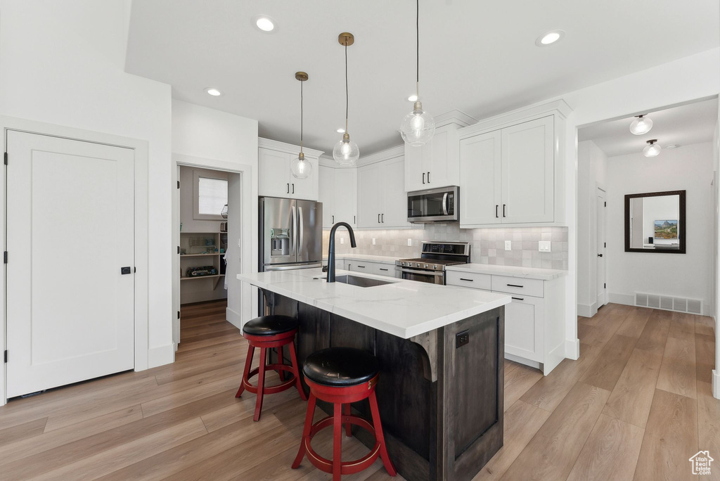 Kitchen with stainless steel appliances, a sink, light wood finished floors, decorative backsplash, and a kitchen breakfast bar
