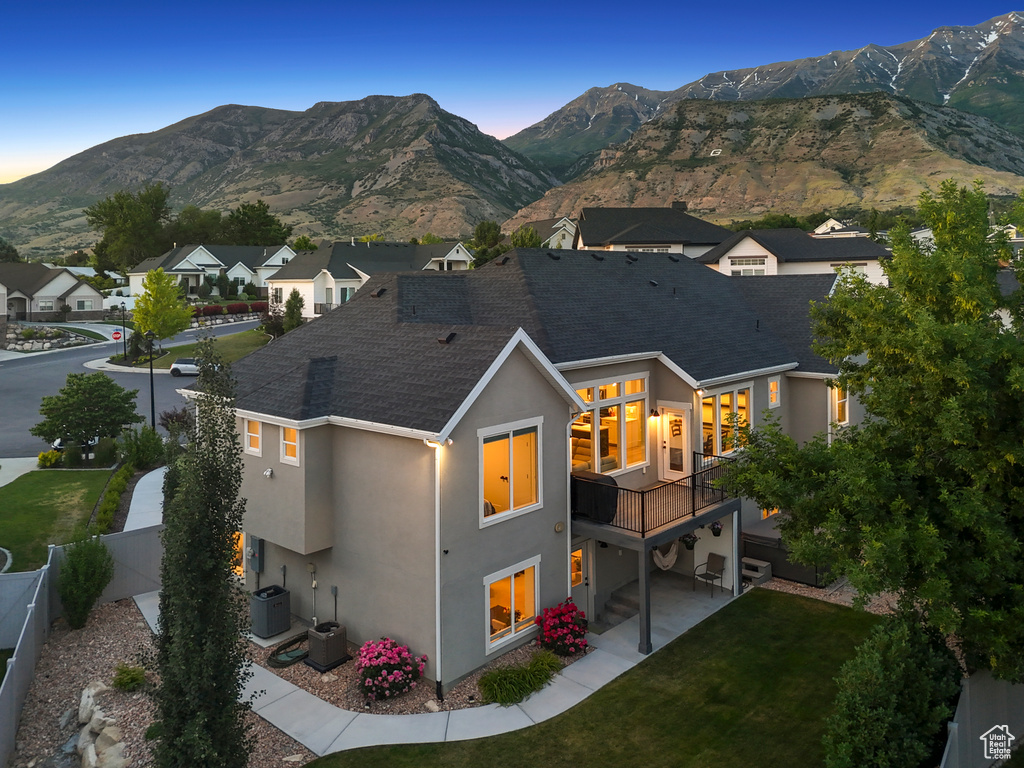 Back of property at dusk with stucco siding, a mountain view, a patio, and roof with shingles