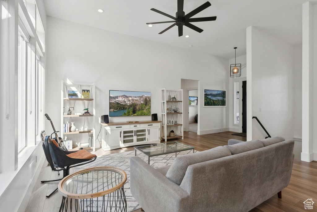 Living area with a high ceiling, ceiling fan, plenty of natural light, wood finished floors, and recessed lighting