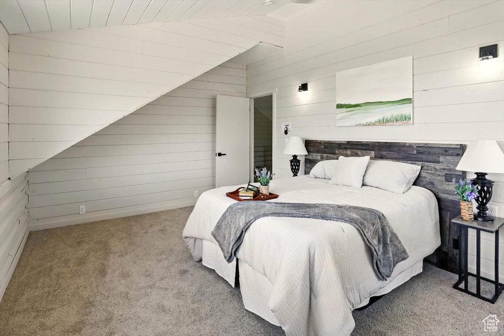 Bedroom with carpet floors, wood walls, and vaulted ceiling