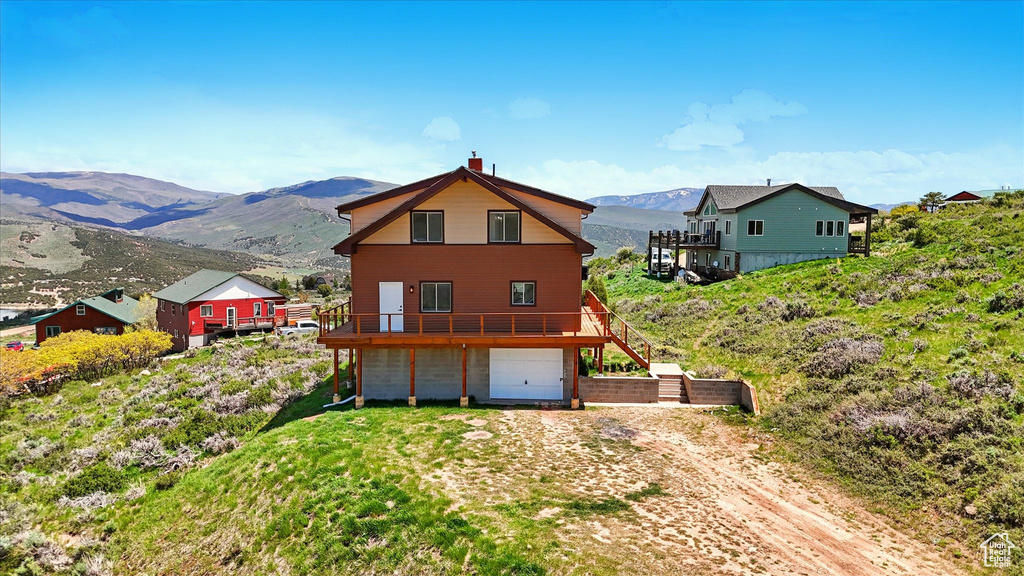 Back of property featuring a garage, a chimney, a deck with mountain view, and driveway