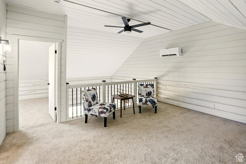 Living area with vaulted ceiling, wood walls, ceiling fan, carpet floors, and a wall unit AC