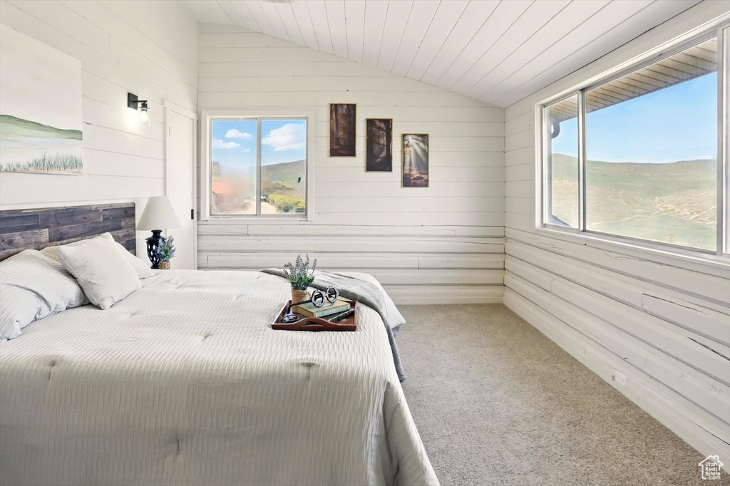 Carpeted bedroom with vaulted ceiling and wood walls
