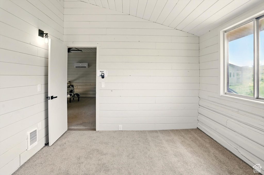 Carpeted empty room with lofted ceiling and wooden walls
