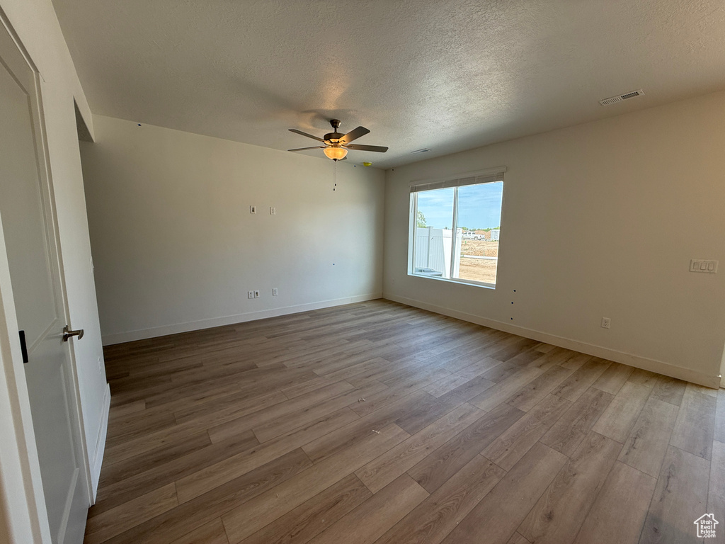Empty room featuring light wood-style floors, a textured ceiling, a ceiling fan, and baseboards