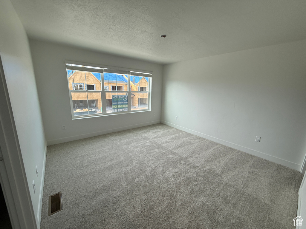 Carpeted spare room featuring baseboards and a textured ceiling