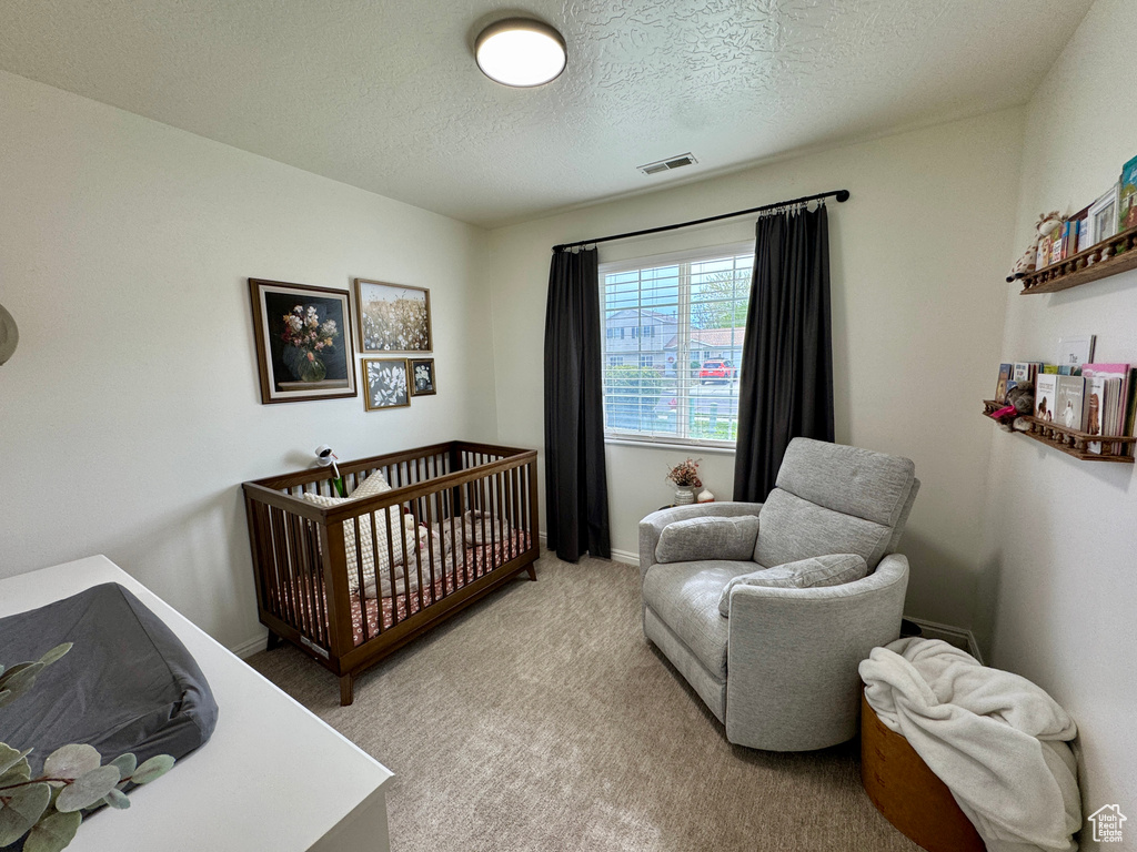 Bedroom featuring light colored carpet, a textured ceiling, and a crib