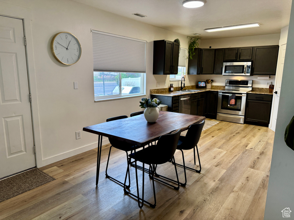 Kitchen featuring stainless steel appliances, a sink, light wood-type flooring, baseboards, and dark cabinetry
