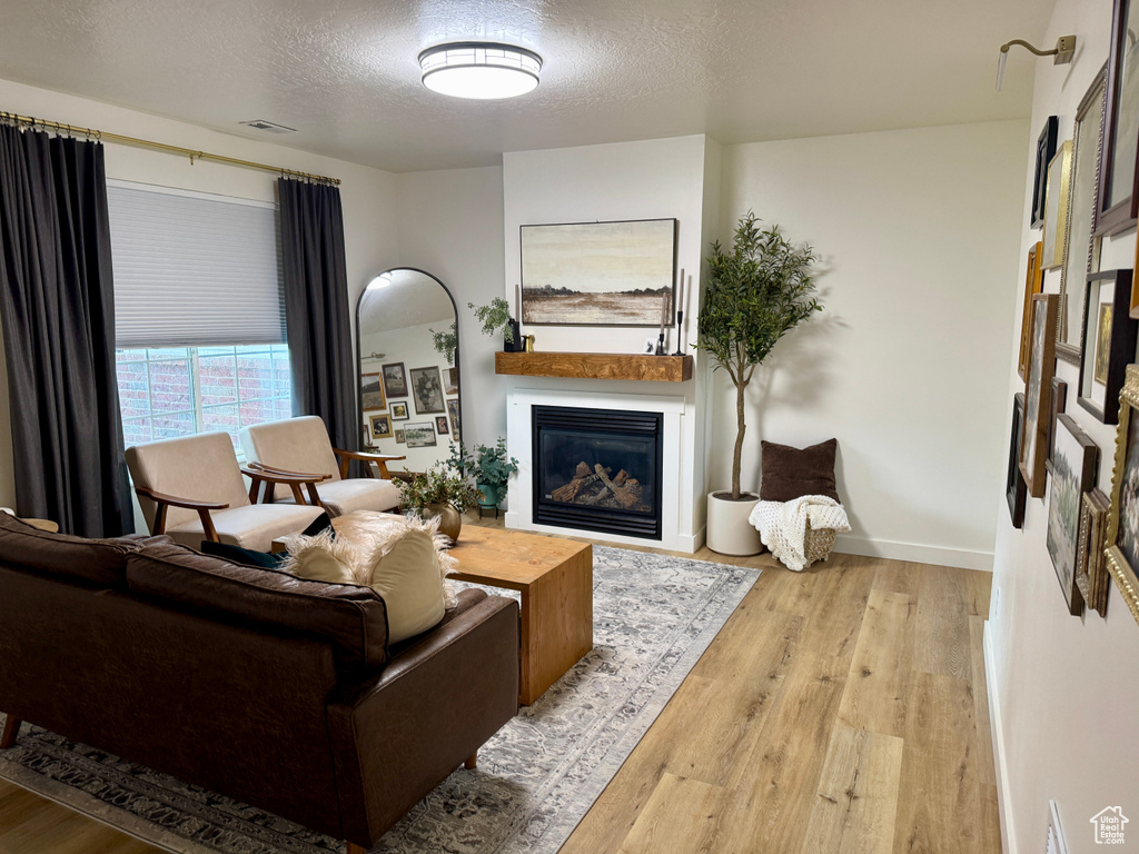 Living room featuring wood finished floors, a glass covered fireplace, a textured ceiling, and baseboards