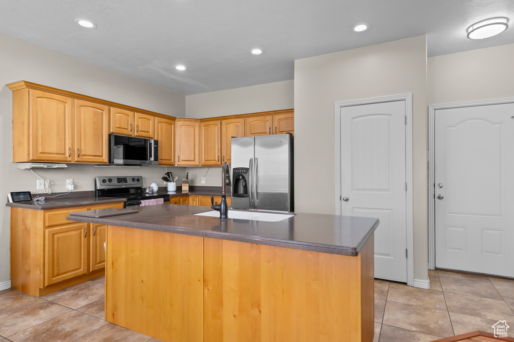 Kitchen featuring appliances with stainless steel finishes, dark countertops, an island with sink, light tile patterned flooring, and recessed lighting