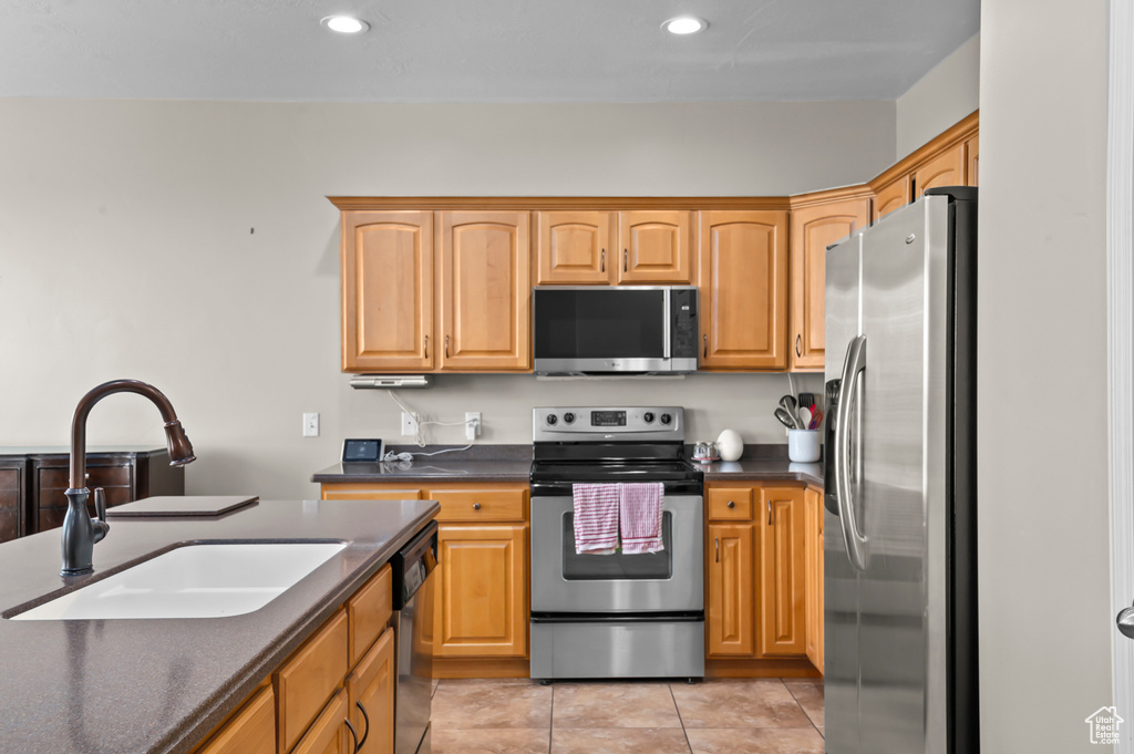 Kitchen featuring stainless steel appliances, a sink, dark countertops, recessed lighting, and light tile patterned floors