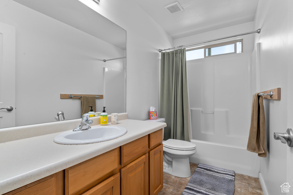 Bathroom featuring vanity, shower / bath combo, toilet, and stone finish floors