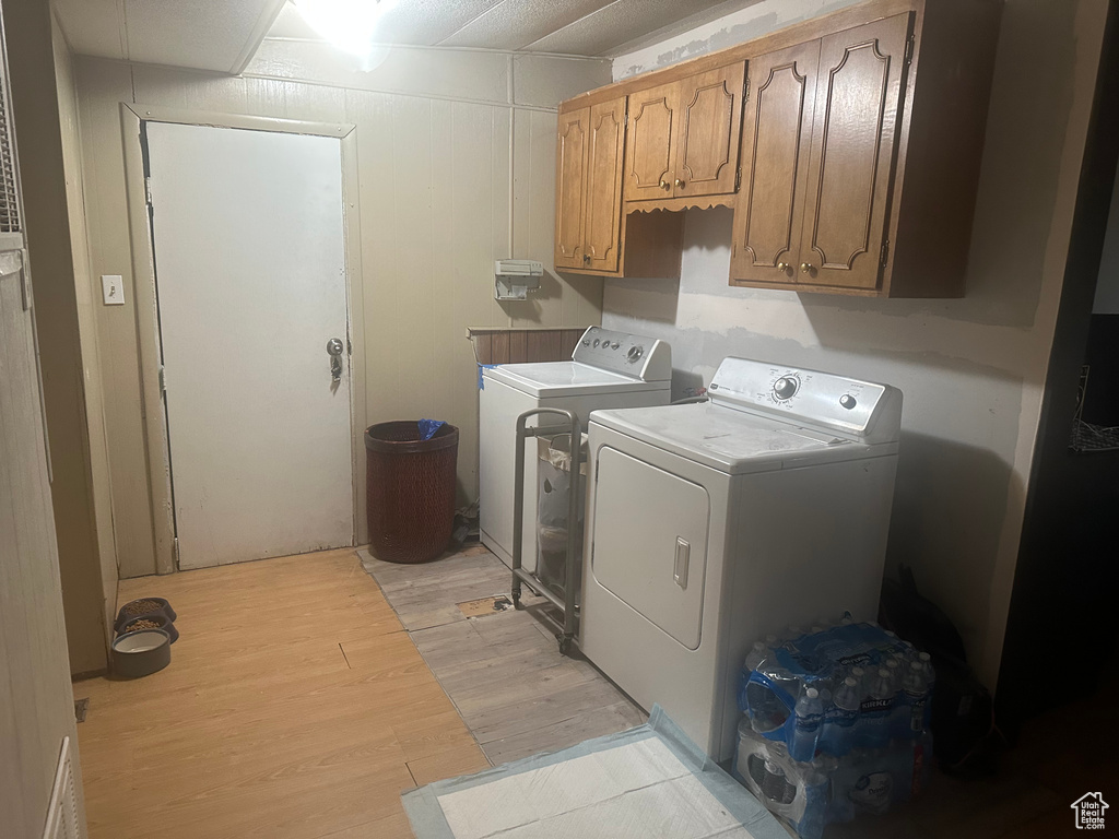 Washroom featuring separate washer and dryer, cabinet space, and light wood finished floors