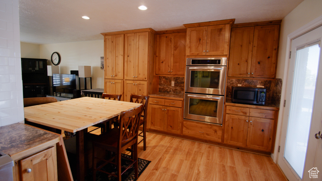 Kitchen featuring double oven, light wood finished floors, brown cabinetry, recessed lighting, and decorative backsplash