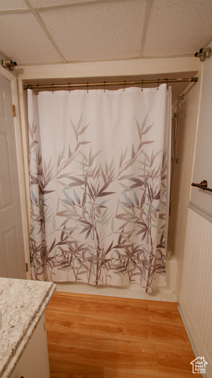 Full bath featuring vanity, wood finished floors, shower / bath combo with shower curtain, and a drop ceiling