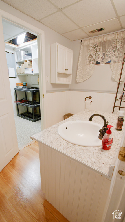Bathroom with a paneled ceiling, vanity, a wainscoted wall, and wood finished floors