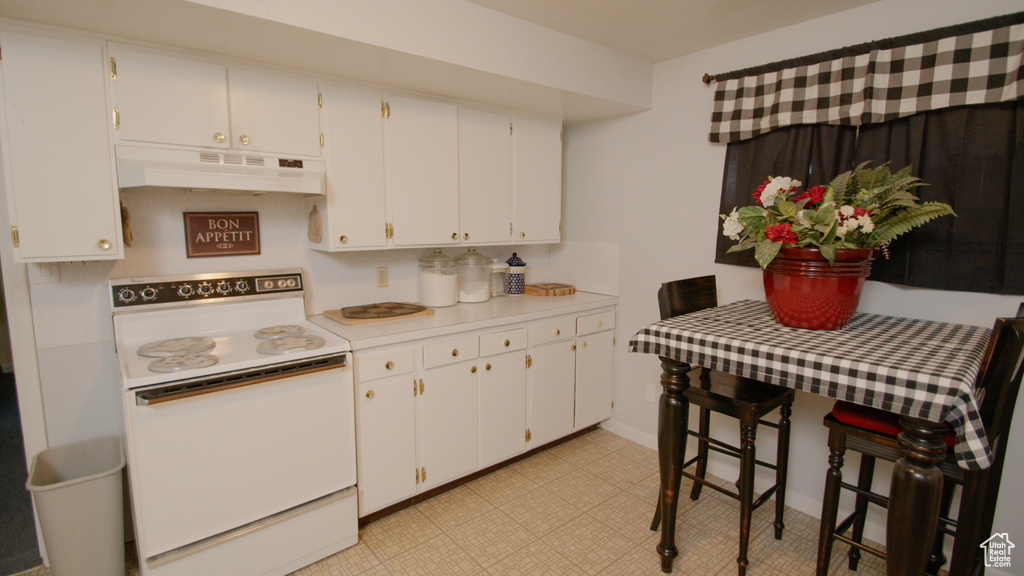 Kitchen with electric stove, extractor fan, light countertops, and white cabinetry