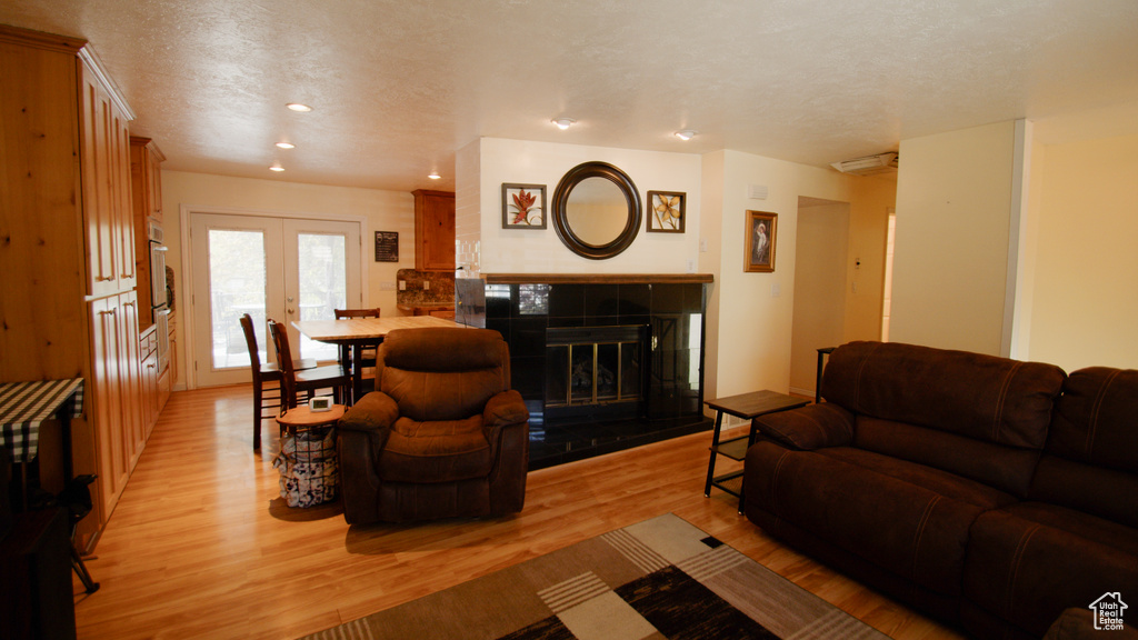 Living area featuring light wood-type flooring, a textured ceiling, french doors, recessed lighting, and a tile fireplace