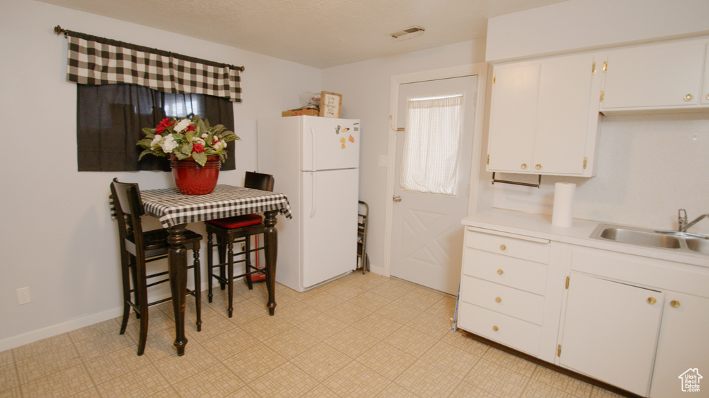 Kitchen with freestanding refrigerator, a sink, white cabinets, and light countertops