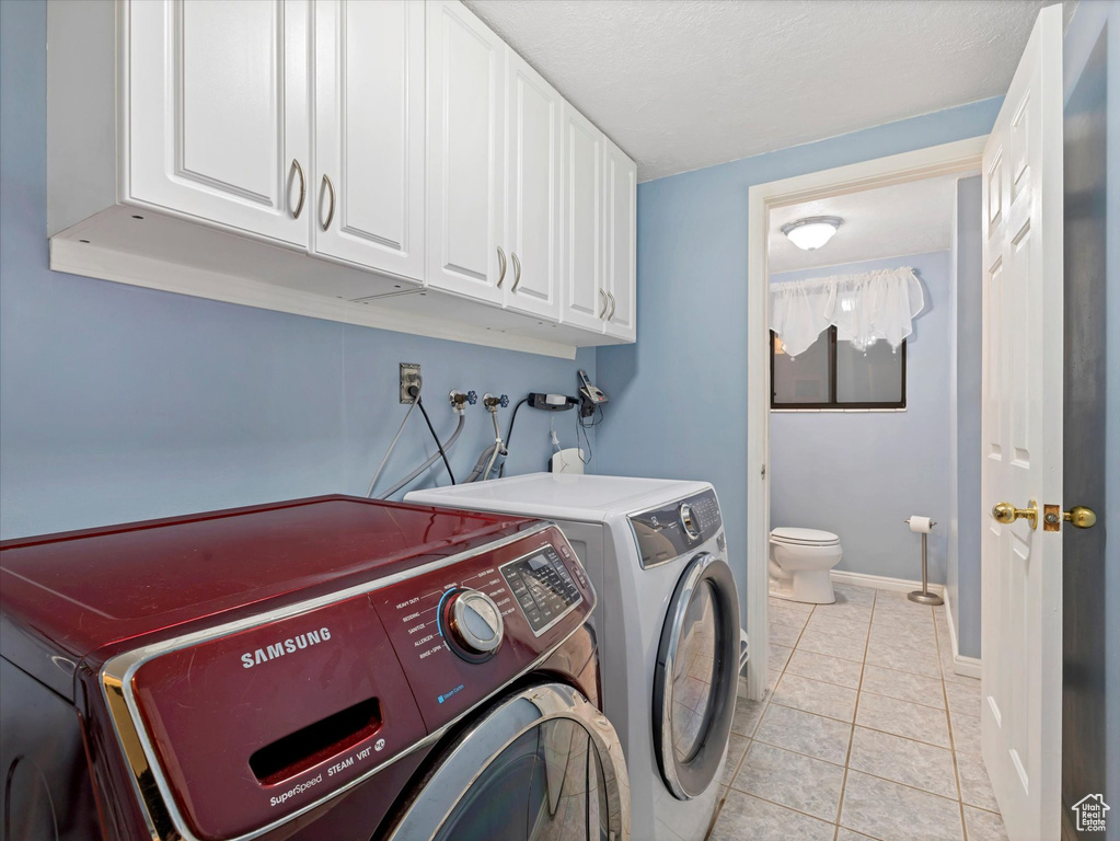 Laundry area with cabinet space, separate washer and dryer, light tile patterned flooring, and baseboards