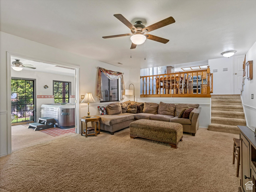 Living area with a ceiling fan, carpet floors, and stairs
