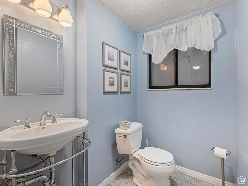 Half bathroom with baseboards, toilet, a sink, a textured ceiling, and tile patterned floors