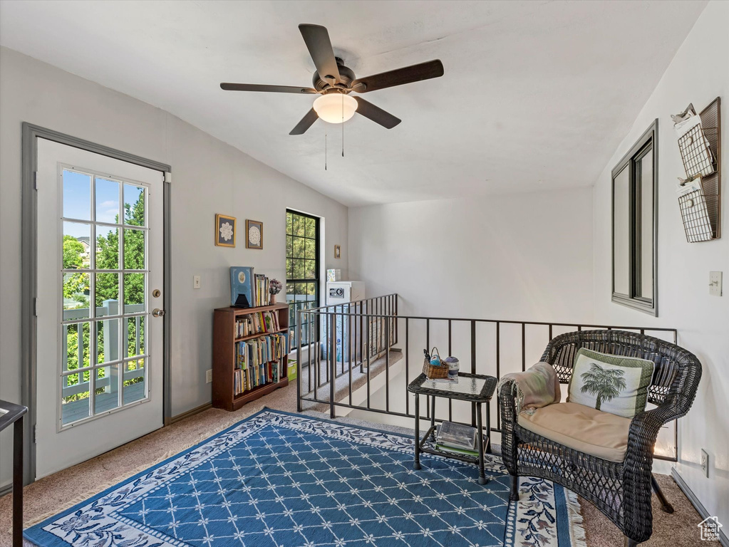 Living area with carpet flooring, a ceiling fan, and an upstairs landing
