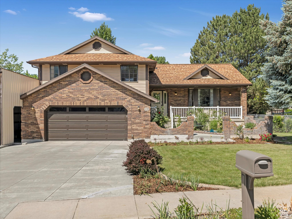 Split level home with brick siding, concrete driveway, a front yard, covered porch, and a garage