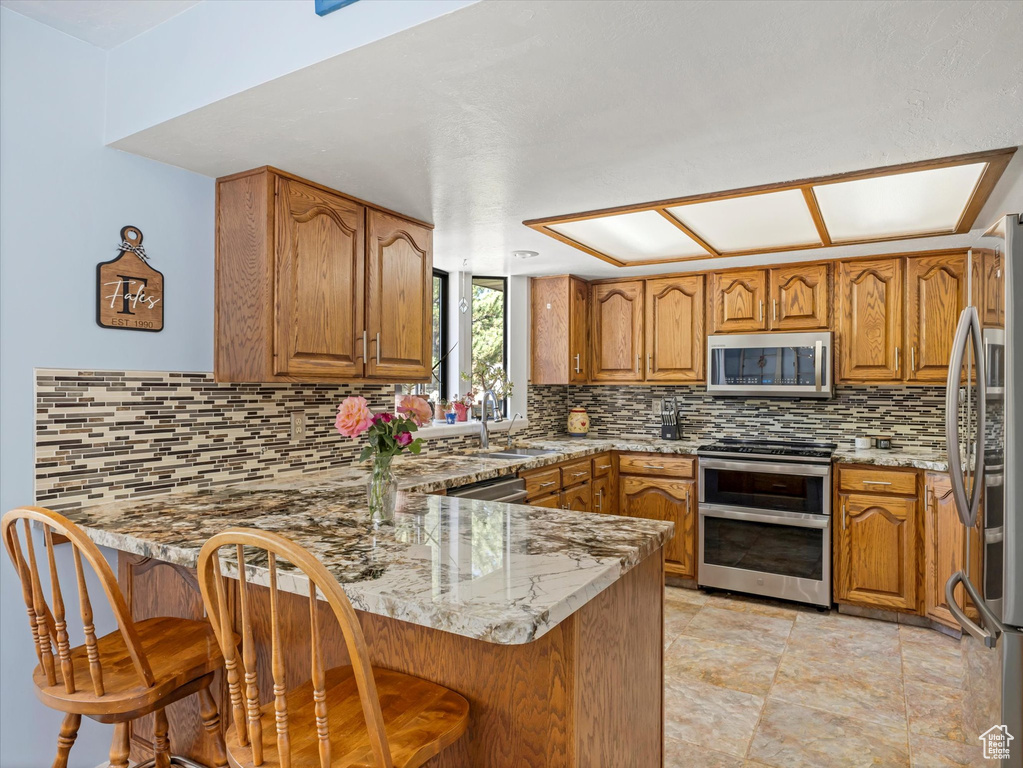 Kitchen with appliances with stainless steel finishes, a peninsula, brown cabinetry, and a sink