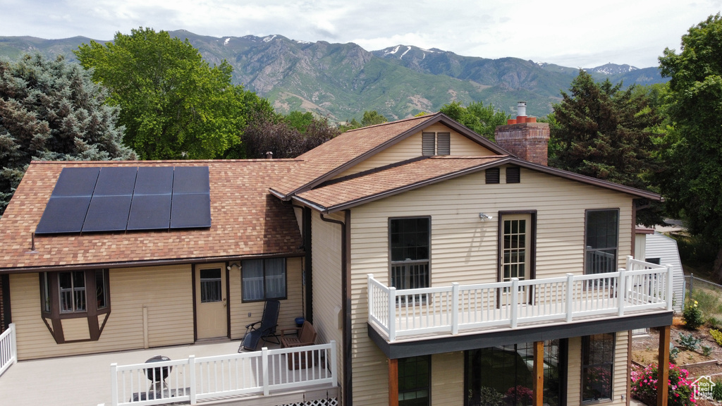 Rear view of property featuring roof mounted solar panels, a chimney, roof with shingles, and a deck with mountain view