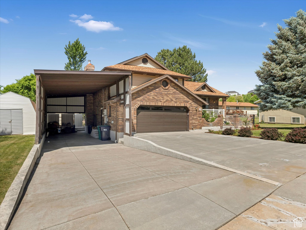 View of front of home featuring brick siding, a carport, a chimney, driveway, and a shed