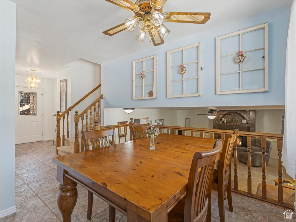 Dining room featuring a ceiling fan, a chandelier, a brick fireplace, and stairs