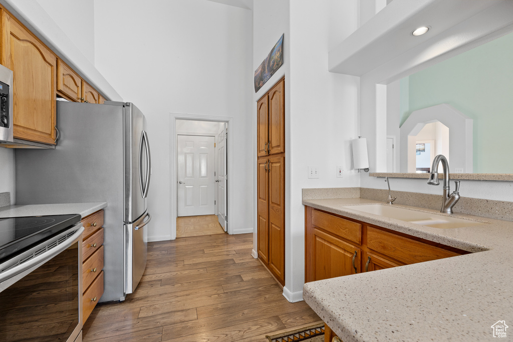 Kitchen with a sink, appliances with stainless steel finishes, light countertops, wood finished floors, and a towering ceiling