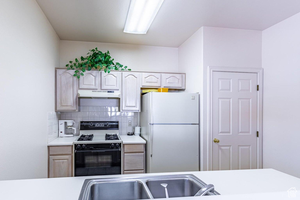 Kitchen with freestanding refrigerator, gas range, under cabinet range hood, light countertops, and backsplash