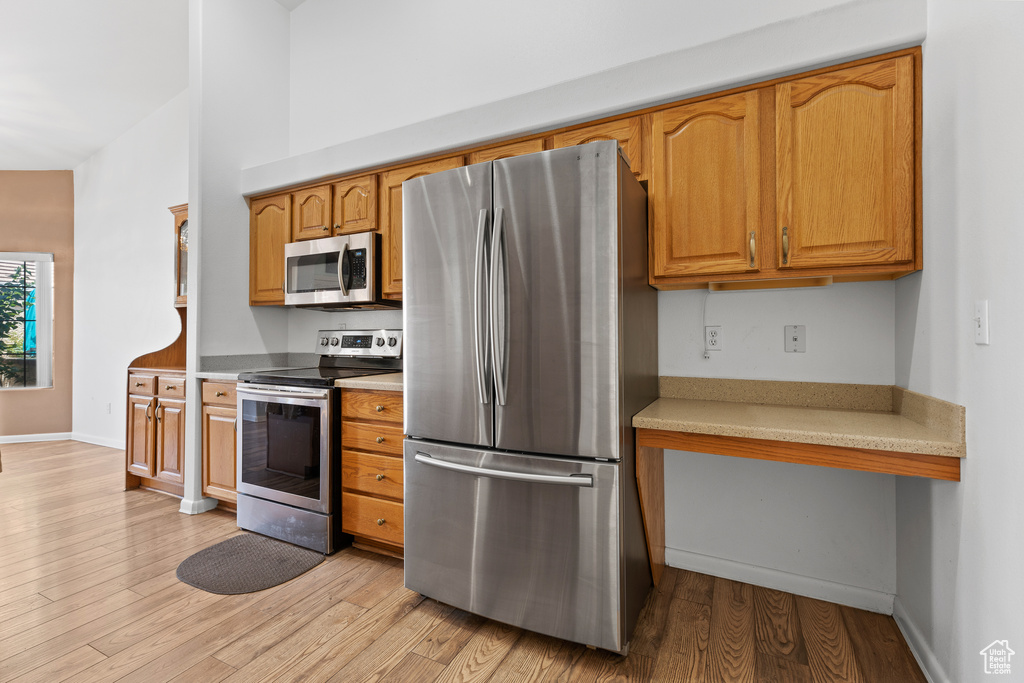 Kitchen with stainless steel appliances, light countertops, light wood-style floors, baseboards, and brown cabinetry