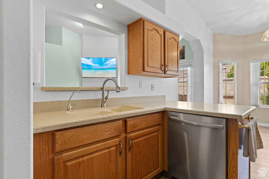 Kitchen with stainless steel dishwasher, a sink, light wood-type flooring, and brown cabinetry