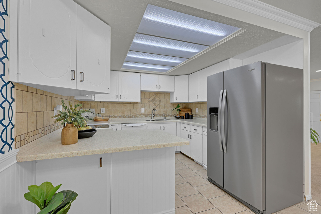 Kitchen featuring stainless steel refrigerator with ice dispenser, a sink, a peninsula, light countertops, and white cabinets