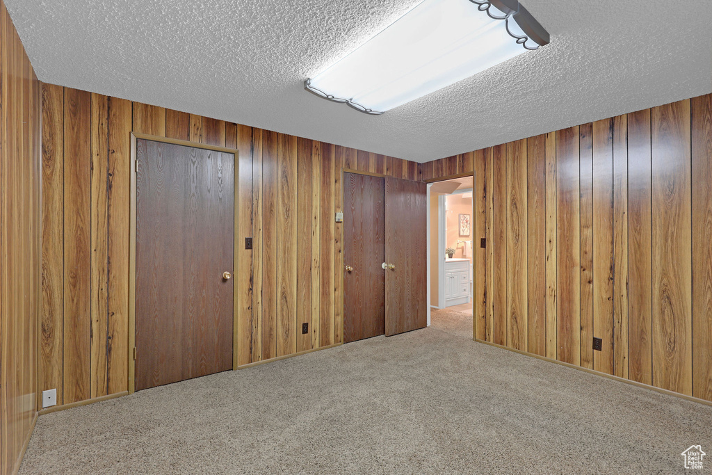 Unfurnished bedroom with a textured ceiling, carpet, wood walls, and two closets