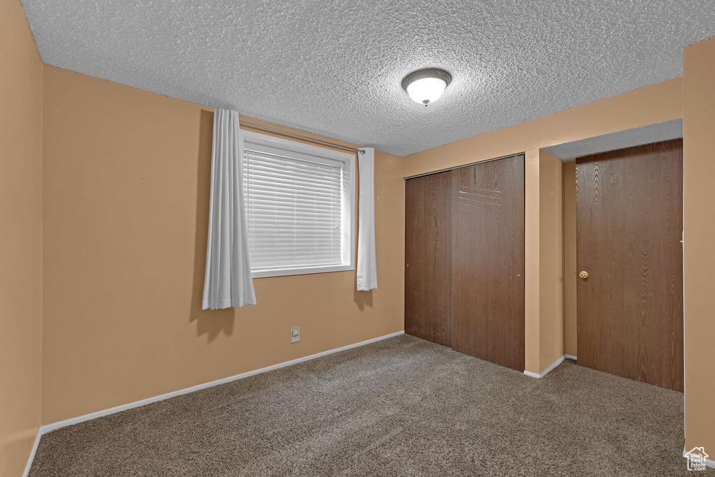 Unfurnished bedroom featuring carpet, a textured ceiling, a closet, and baseboards