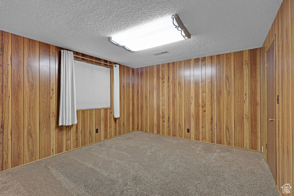 Carpeted spare room with a textured ceiling and wooden walls