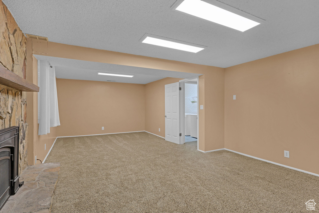 Unfurnished living room featuring light colored carpet, a wood stove, and baseboards