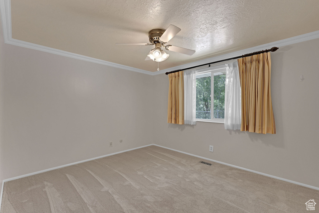 Empty room featuring crown molding, a ceiling fan, baseboards, light colored carpet, and a textured ceiling