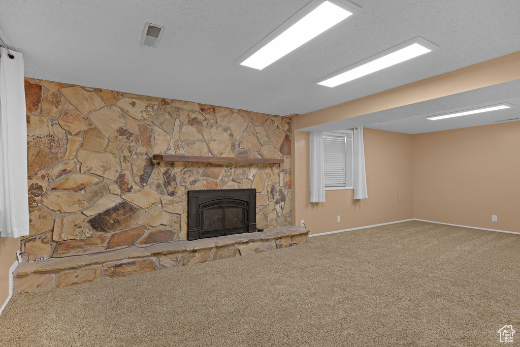 Unfurnished living room featuring carpet floors, baseboards, and a stone fireplace
