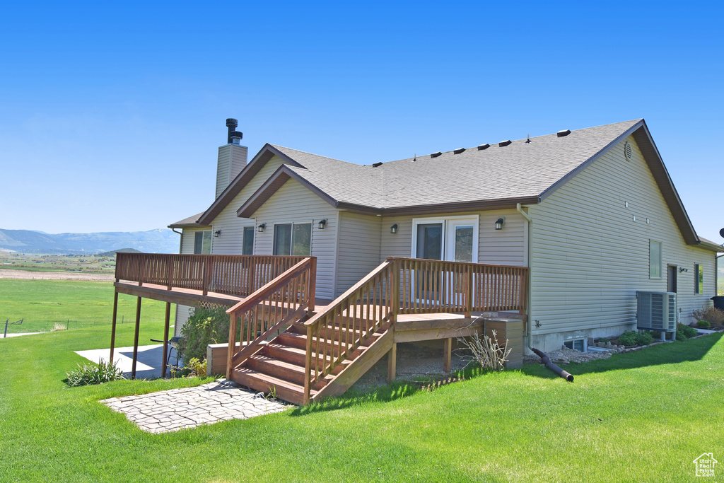 Back of house with a patio, a deck with mountain view, a chimney, cooling unit, and a yard