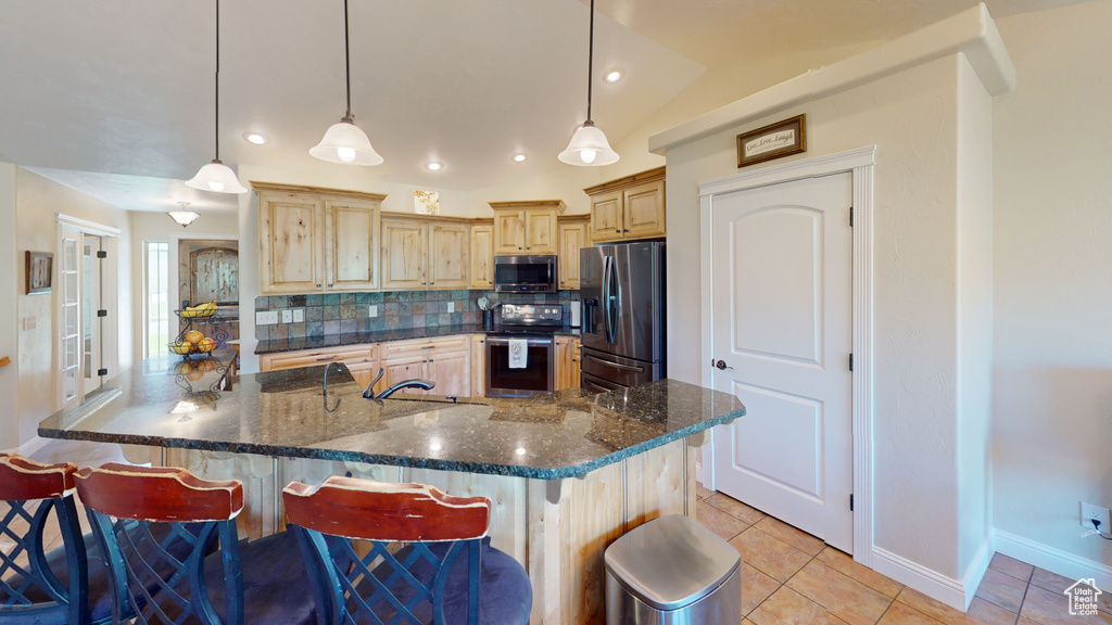 Kitchen featuring stainless steel appliances, light brown cabinetry, light tile patterned floors, decorative backsplash, and a kitchen breakfast bar