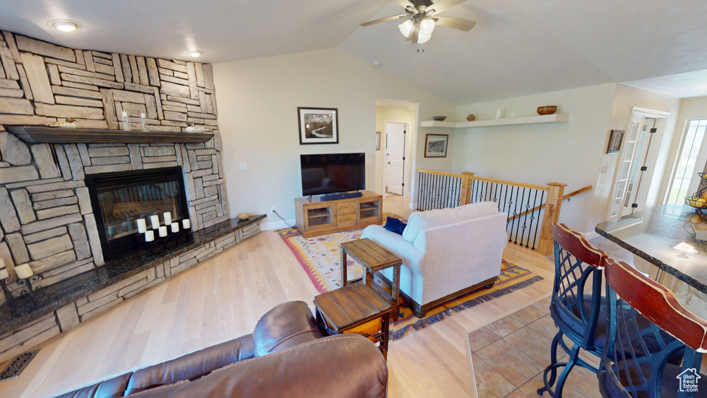 Living room featuring ceiling fan, lofted ceiling, wood finished floors, and a stone fireplace