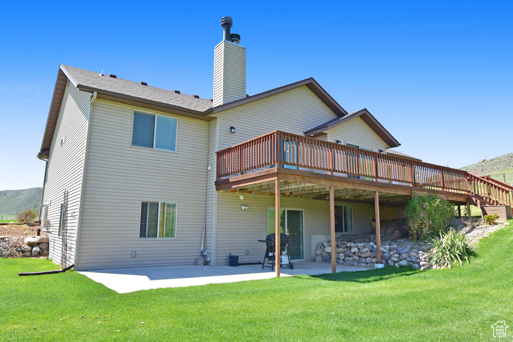 Back of property featuring a deck, a patio area, a yard, and a chimney