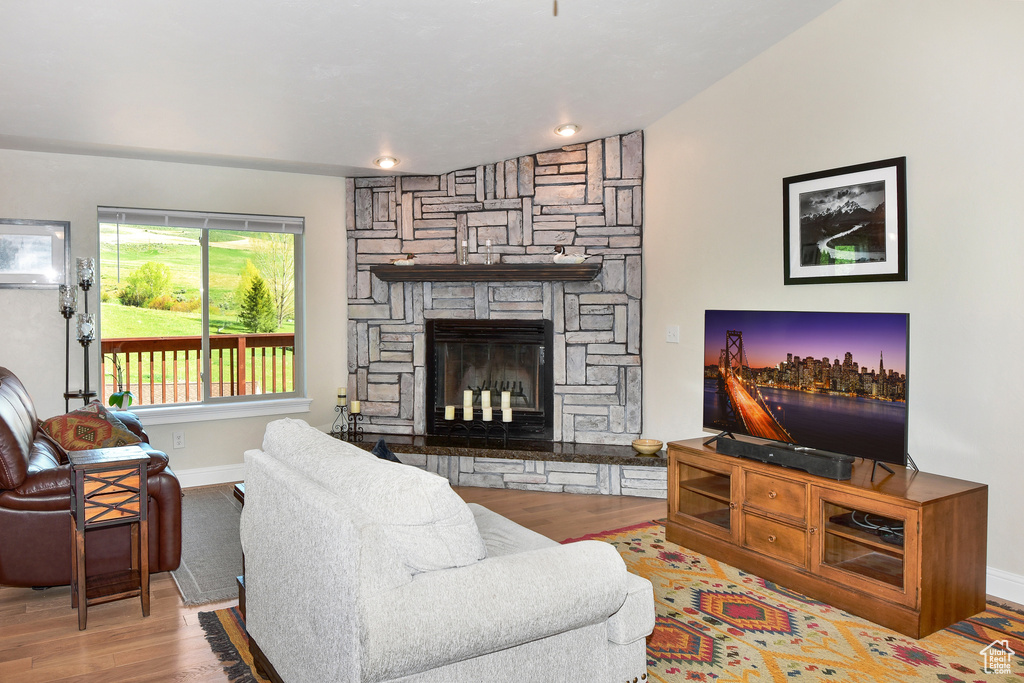 Living room featuring wood finished floors, baseboards, a stone fireplace, and lofted ceiling