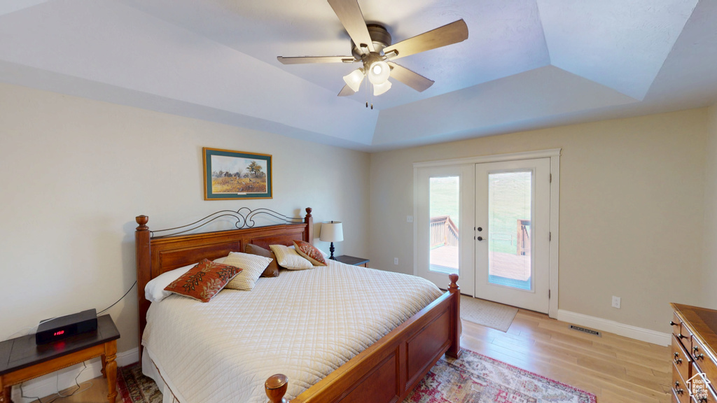 Bedroom featuring a raised ceiling, access to exterior, french doors, light wood-style flooring, and a ceiling fan