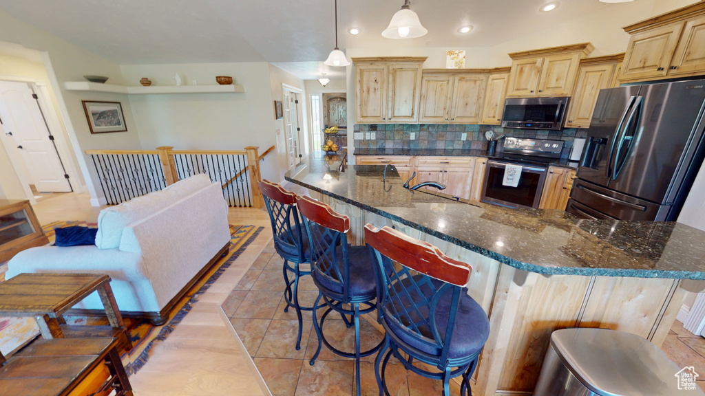 Kitchen with stainless steel appliances, light brown cabinetry, decorative backsplash, recessed lighting, and a breakfast bar area